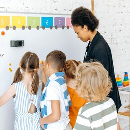 Kinder und eine Erwachsene pinnen gemeinsam Zettel an ein Whiteboard