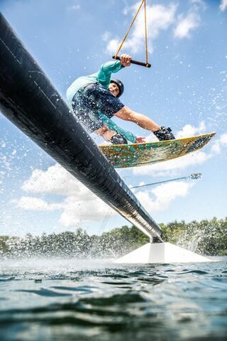 Das Bild zeigt einen Wakeboard-Fahrer, der über eine Stange über dem Wasser fährt.